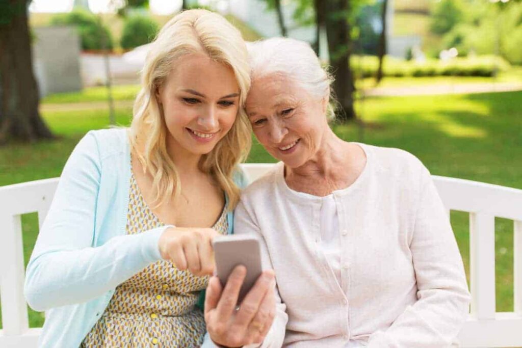 Senior woman sitting outdoors on a bench with her daughter looking at information for Traditions of Zanesville on a smartphone