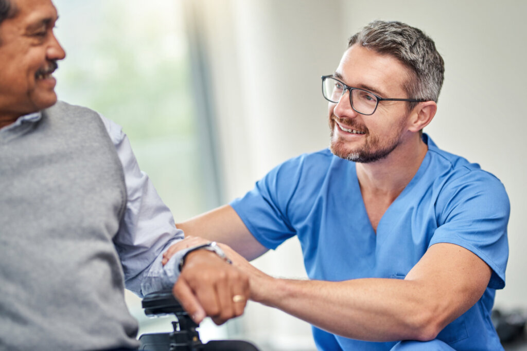 Male nurse smiling and patting the arm of a memory care resident at Traditions of Zanesville in Zanesville, OH.