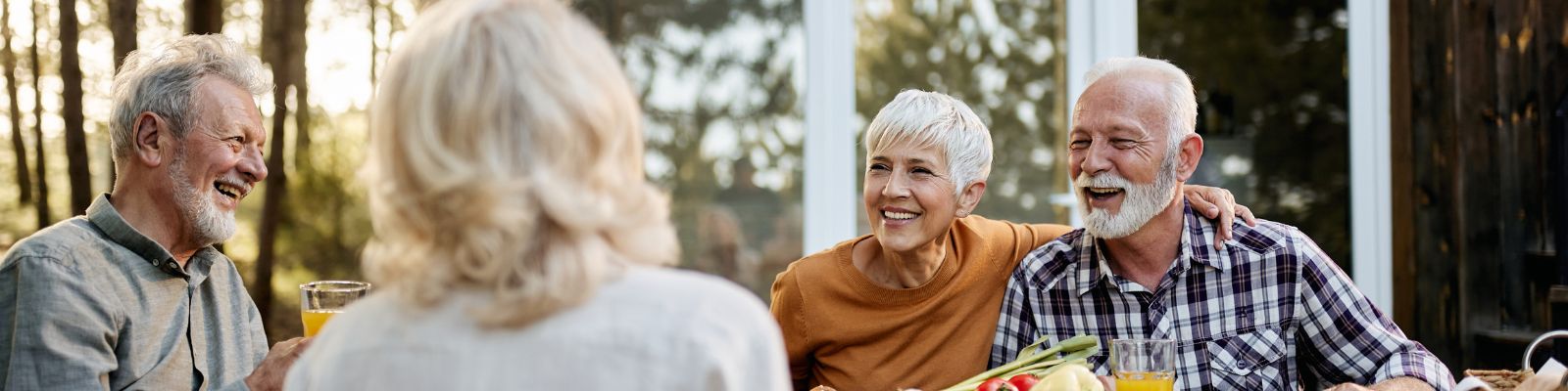 a group of two senior men and two senior women sitting down laughing and smiling at each other outside