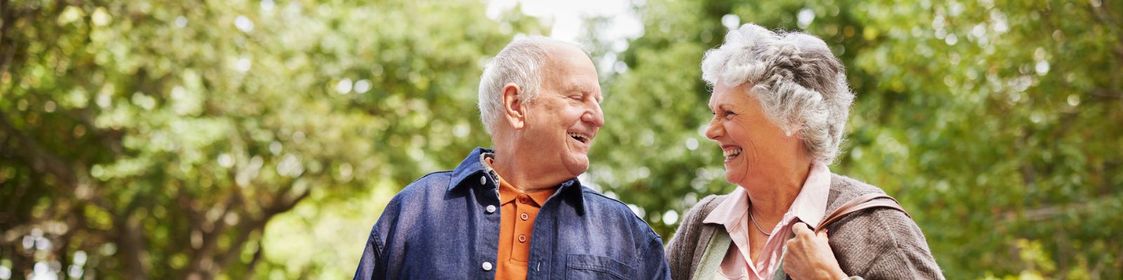 A senior man and senior woman walking side by side, looking at each other smiling and laughing
